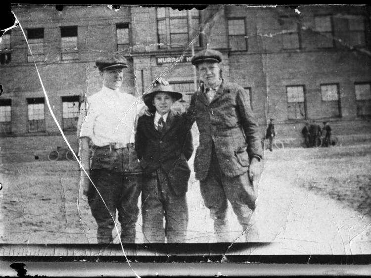 Tre män framför en tegelbyggnad.